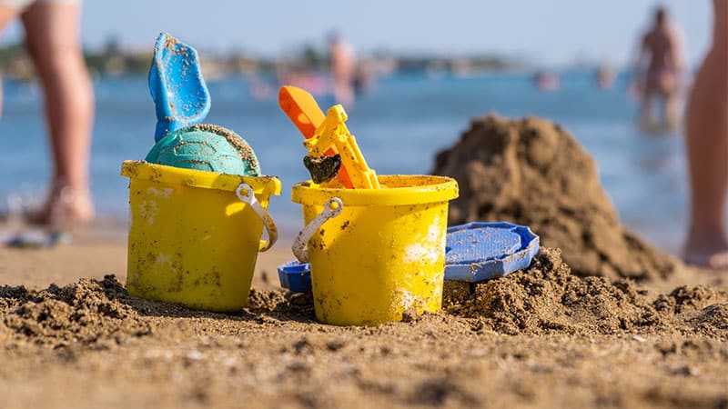 Two yellow sand castle buckets on Skegness Beach, with happy people enjoying the ocean in the background. Experience seaside fun with a Kingfisher caravan for rent Skegness