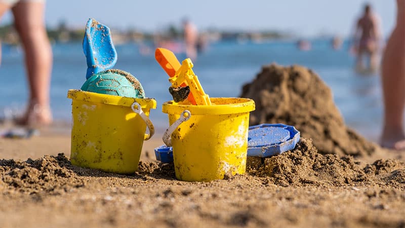 Two yellow sand castle buckets on Skegness Beach, with happy people enjoying the ocean in the background. Experience seaside fun with a Kingfisher static caravan holidays.