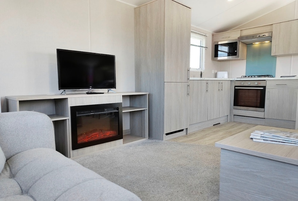 Modern static caravan lounge with TV, electric fire and fitted kitchen at Kingfisher Caravan Park