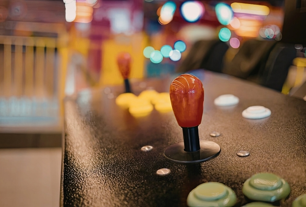 Close-up of an orange arcade joystick and buttons with colourful lights behind