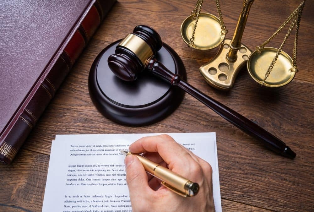 A close-up of a hand signing a static caravan purchase agreement or site license contract on a wooden desk next to a judge’s gavel and scales of justice