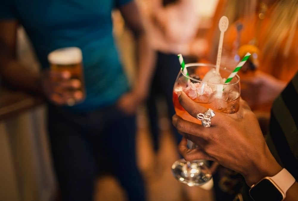 Close-up of a hand holding a pink cocktail with ice and green-and-white striped straws at Fantasy Island Skegness theme park