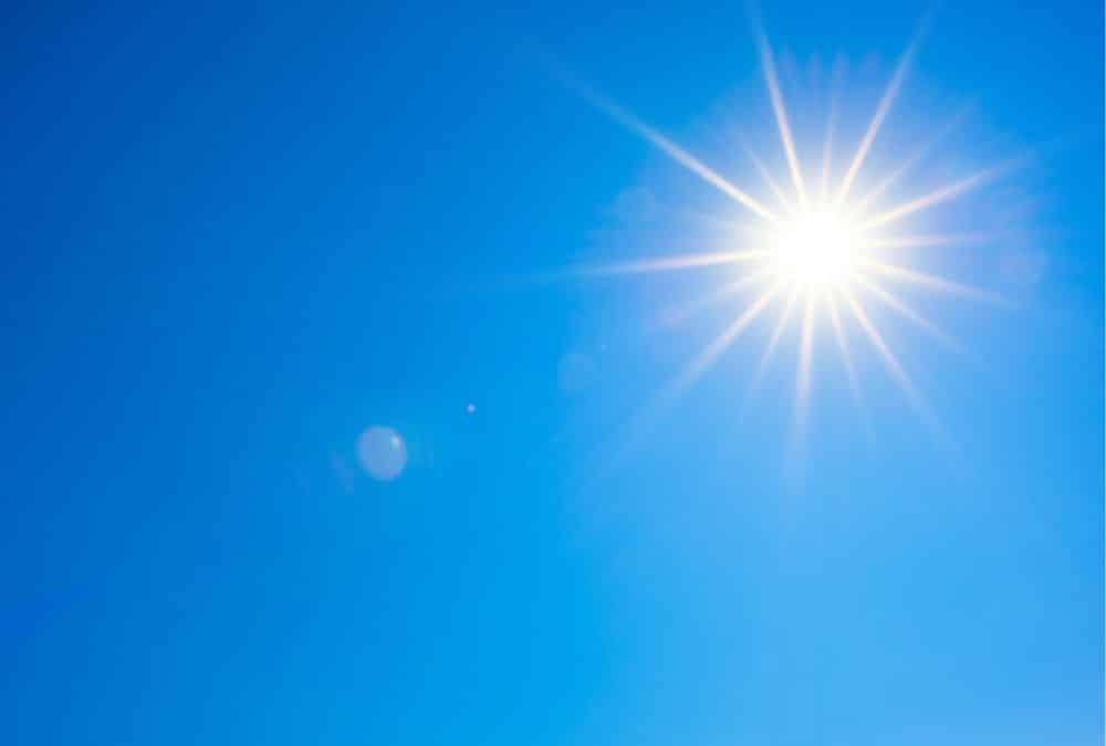 Bright sun in a clear blue sky on a sunny day, with sun rays extending outward.