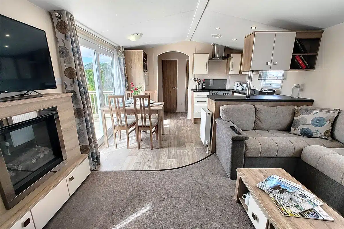 Living room of Premium Plus 3 Bedroom Caravan featuring a 40-inch Smart TV, dining table with tableware, and an electric fireplace for a cosy and modern atmosphere.
