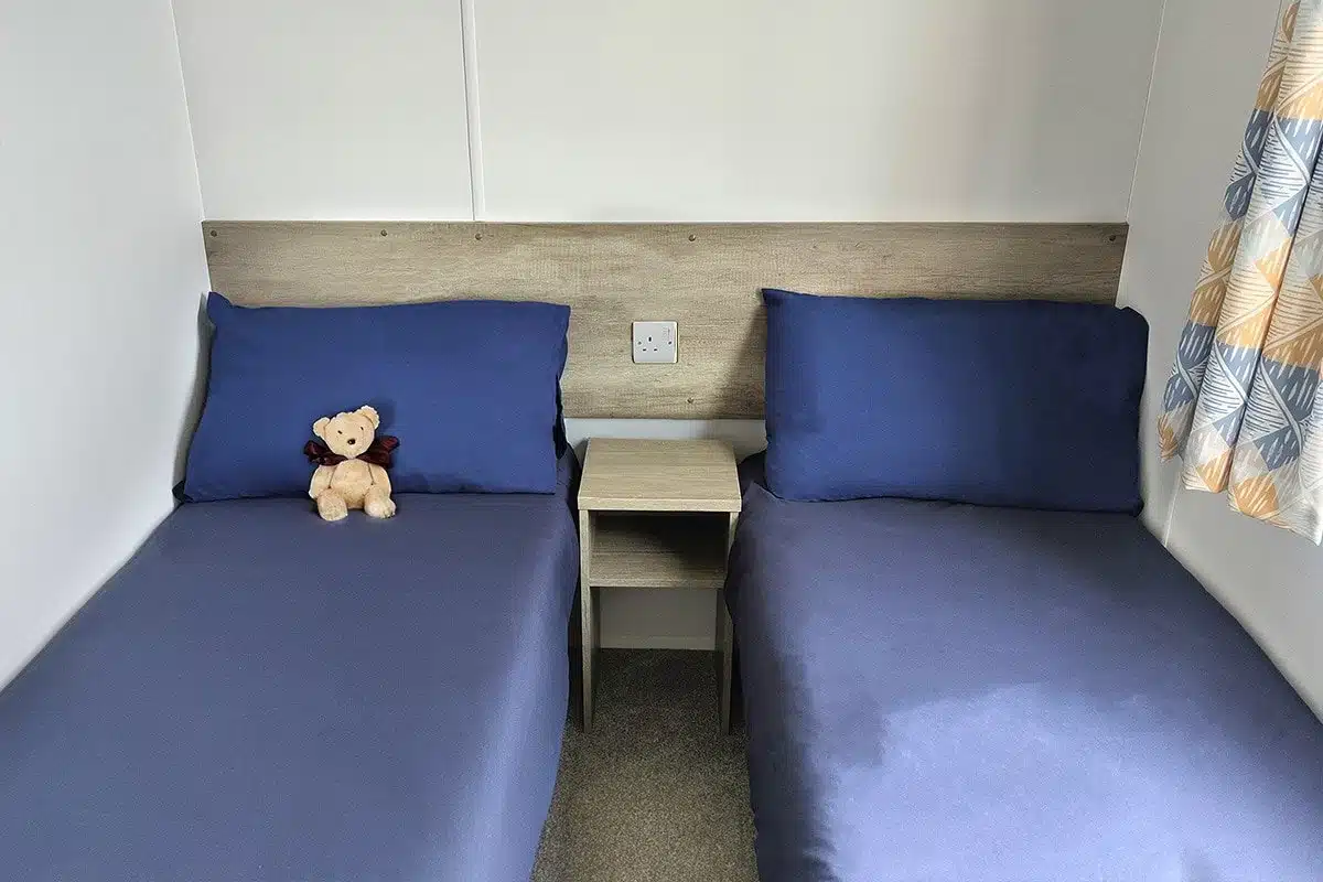 Guest bedroom in a Standard 3 Bedroom Caravan with two single beds, offering space and comfort for a peaceful sleep.