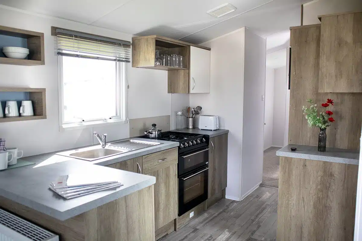 Kitchen in a Standard 3 Bedroom Caravan, equipped with a fridge, gas oven and grill, and tableware for easy meal preparation.