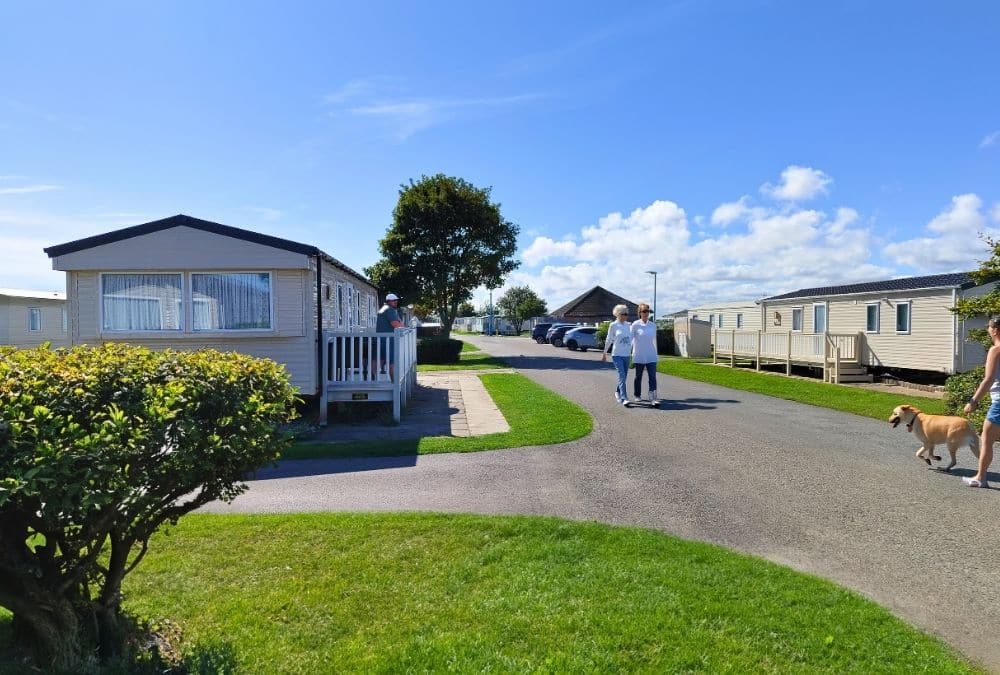 People walking through a static caravan park with holiday homes, green space and a dog