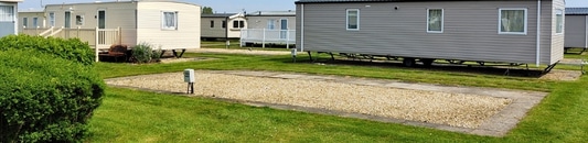 Row of manufactured homes on a grassy lot with gravel driveways in a mobile home park in the suburbs.