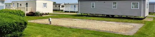 Row of manufactured homes on a grassy lot with gravel driveways in a mobile home park in the suburbs.