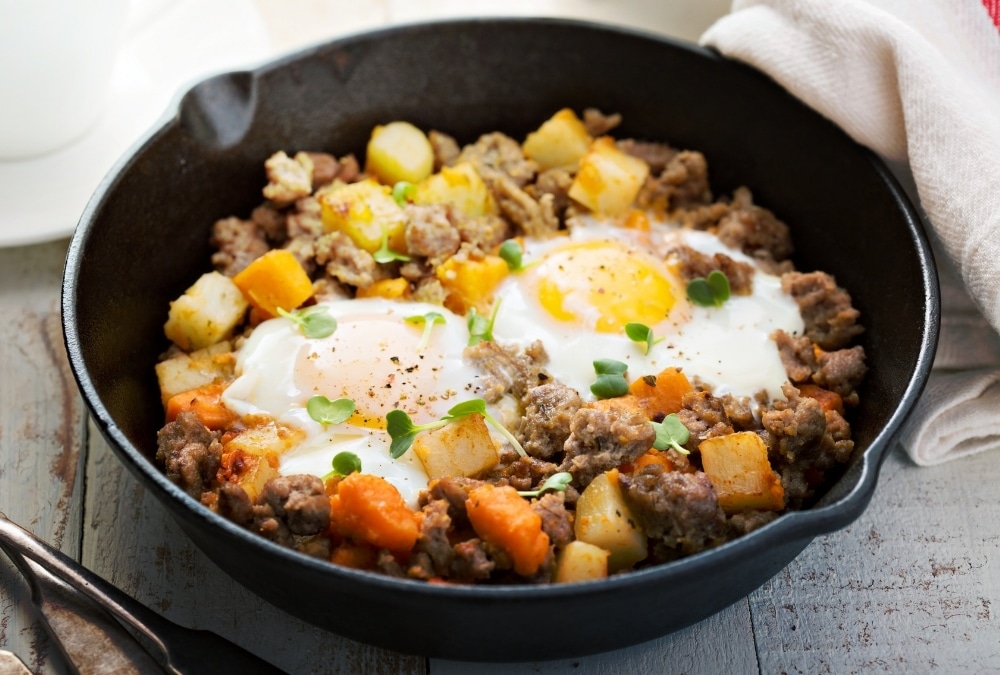 Cast iron pan of breakfast hash with sausage, potato, sweet potato and fried eggs