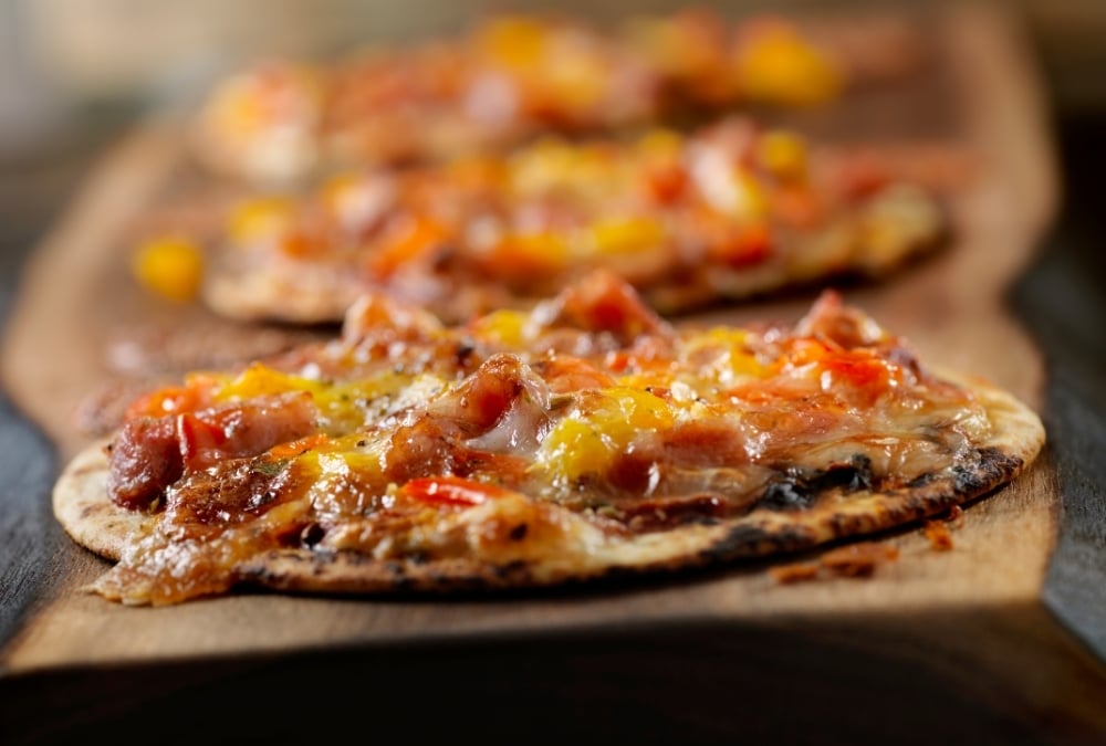 Close-up of tortilla pizzas topped with cheese, bacon and peppers on a wooden board